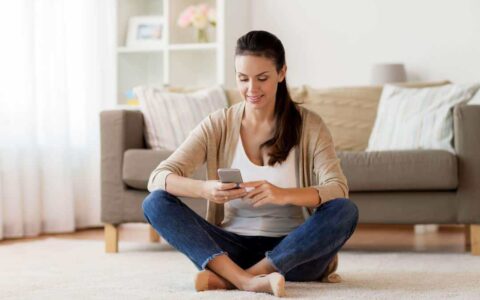 Woman sitting in lounge looking at her phone and smiling