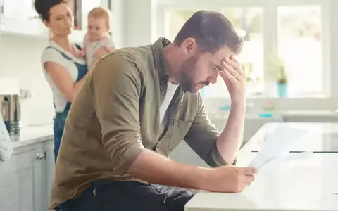 Worried looking father inspecting paper work with wife and baby in the background