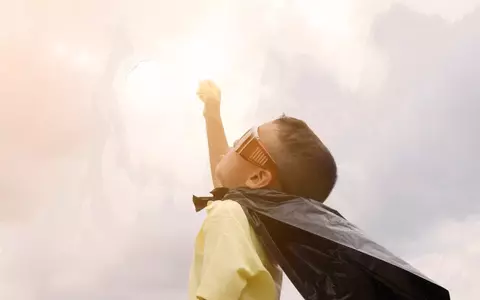 Young boy with cape and glasses pretending to fly