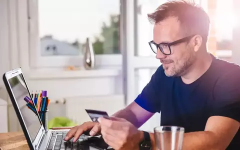 Man smiling at computer with credit card in hand