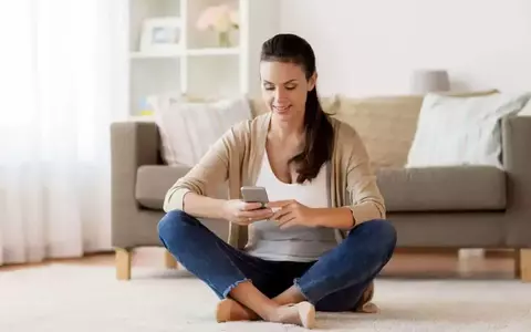 Happy Young Woman Sitting On Floor And Texting Message On Smartphone